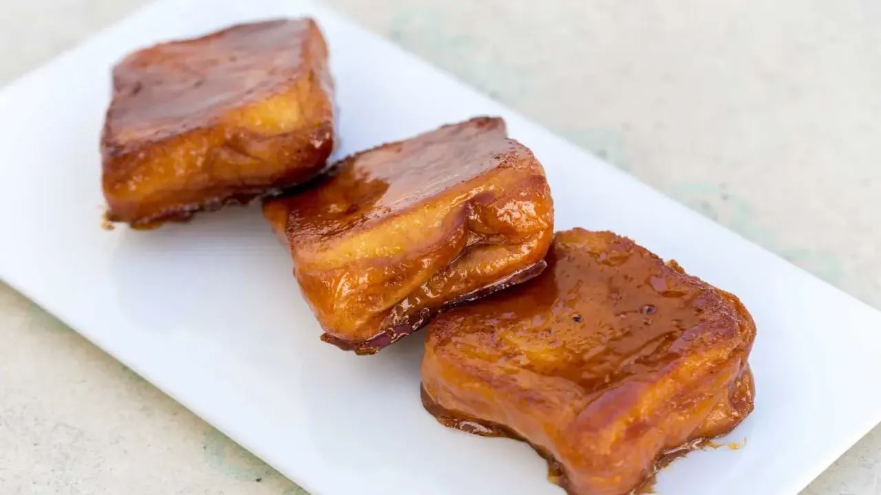 Tres torrijas de miel, doradas y brillantes, reposan en un plato blanco.