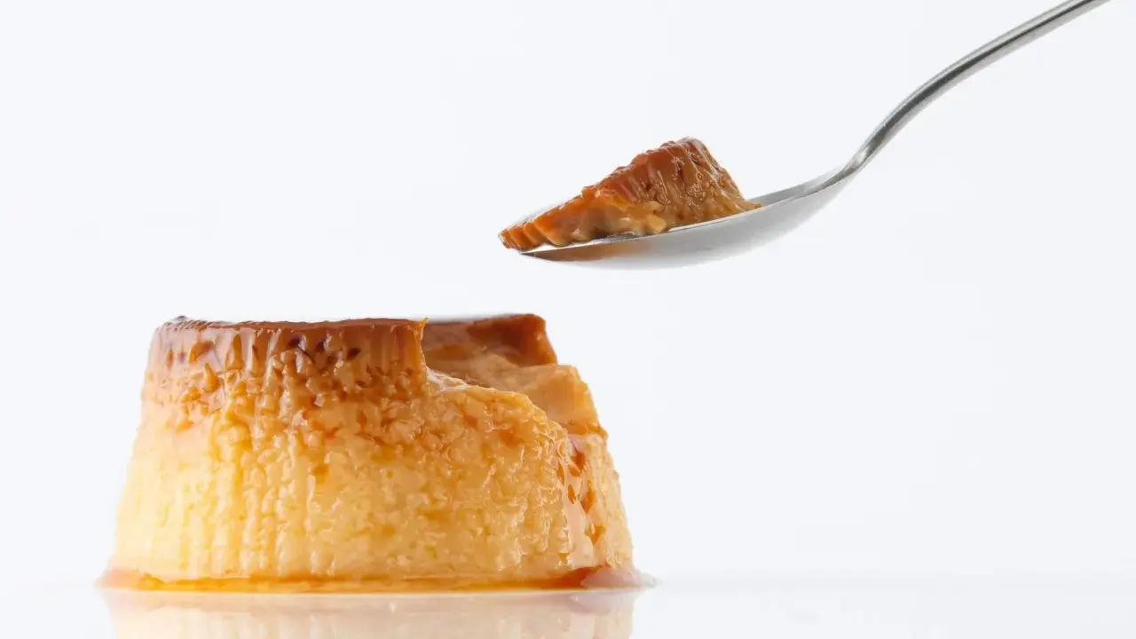 Un trozo de flan casero sin horno en una cuchara, con el resto del postre caramelizado al lado.