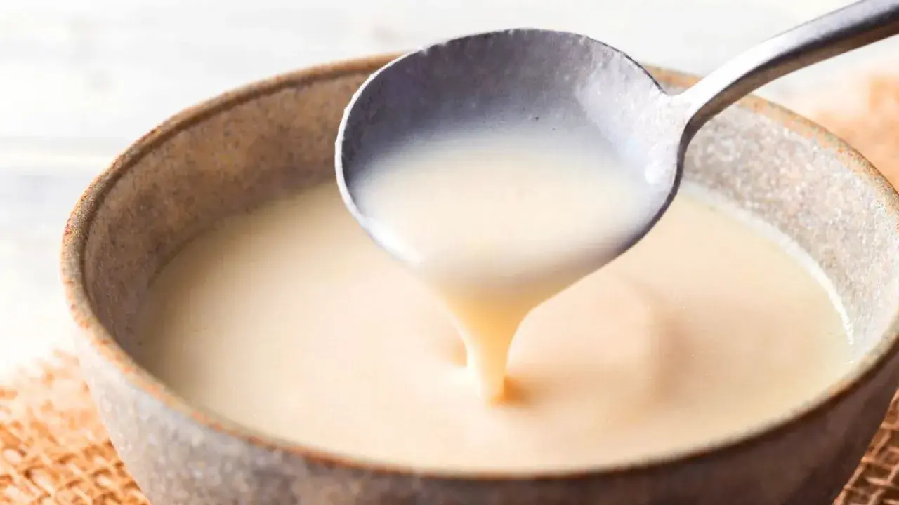 Cuchara sirviendo crema inglesa espesa y suave en un cuenco rústico.