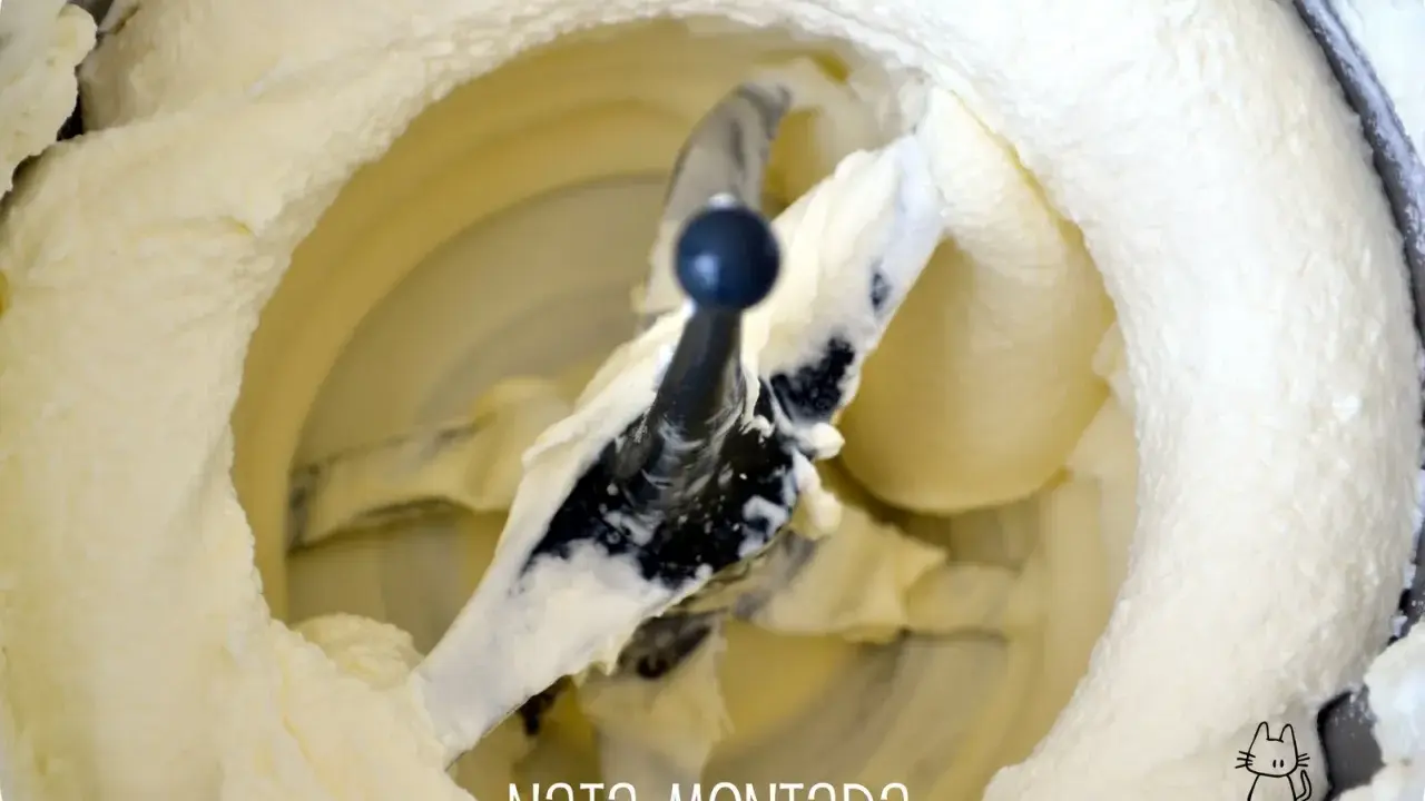 Batidora con pala mezclando nata montada, creando una textura esponjosa y cremosa, lista para postres.