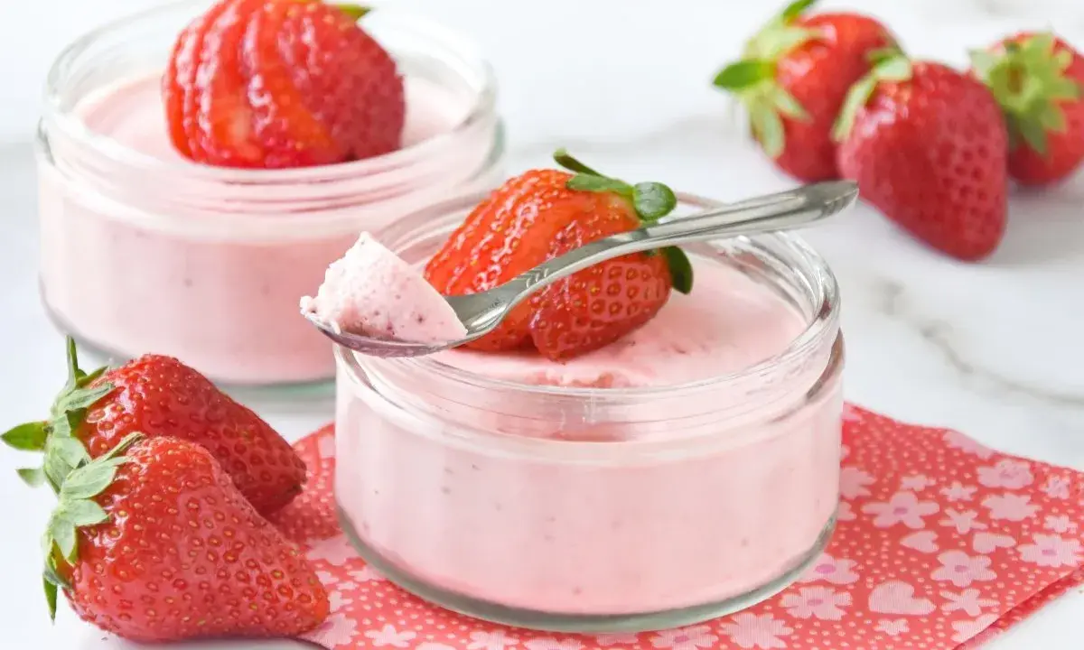 Delicioso postre con fresas, cremoso y ligero, servido en frascos de vidrio. Una fresa fresca corona cada porción.