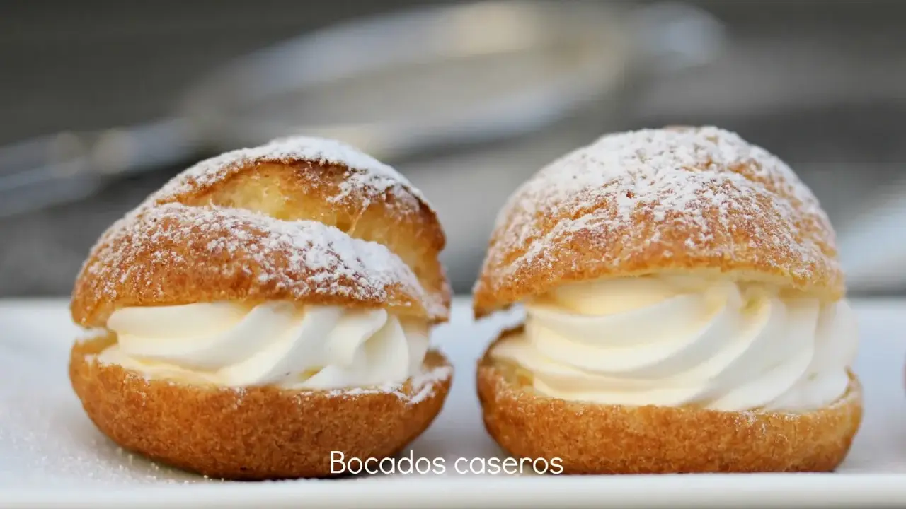 Dos bocados caseros de pasta choux, rellenos de crema batida y espolvoreados con azúcar glas.