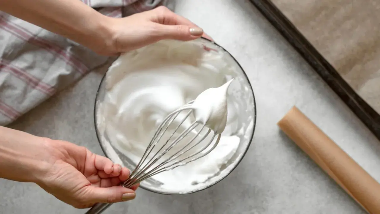 Manos batiendo claras a punto de nieve para un merengue suizo perfecto.