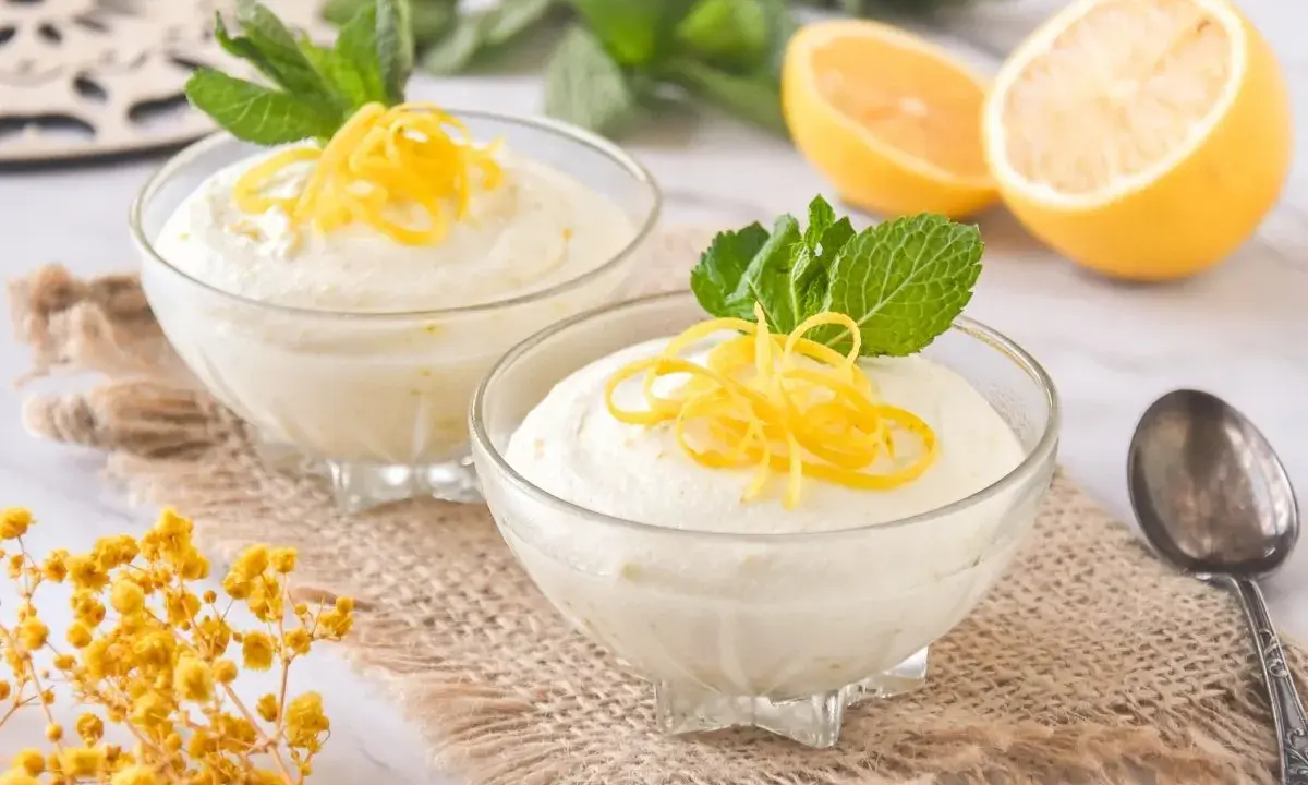 Dos copas de cremoso mousse de limón con leche condensada, decoradas con ralladura de limón y menta.