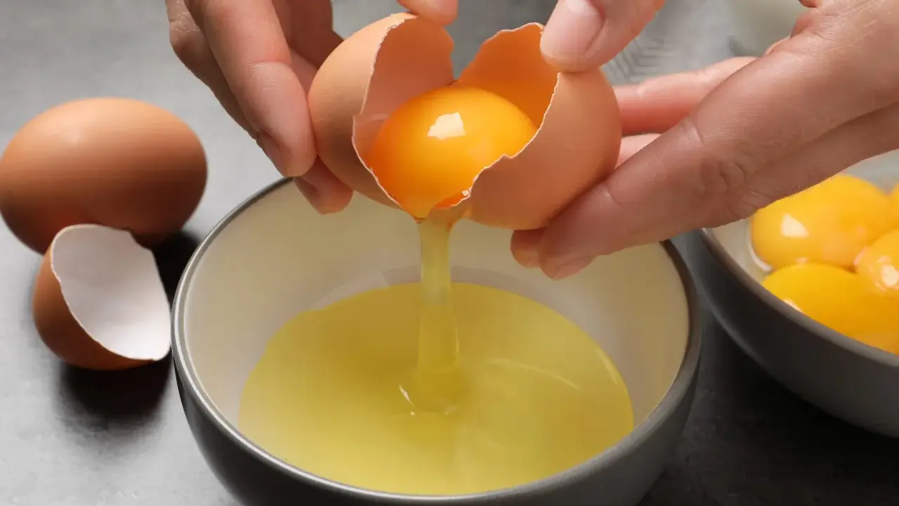 Manos separando la yema de la clara de un huevo. Ideas para saber qué hacer con claras de huevo y yemas.