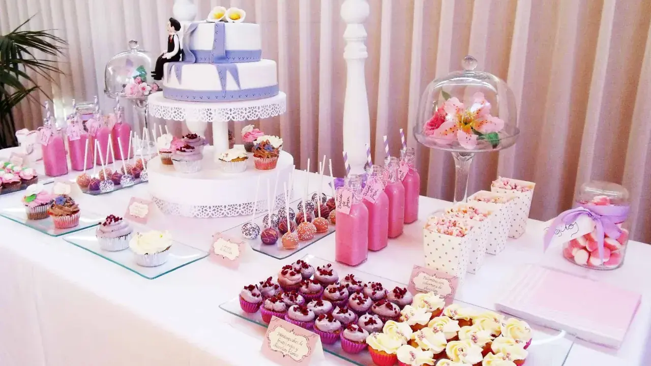 Mesa dulce para 50 cumpleaños con pastel de dos pisos, cupcakes, cake pops, bebidas rosas y palomitas.