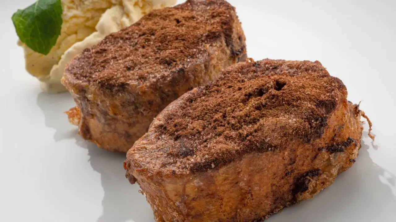 Dos torrijas de chocolate espolvoreadas con cacao y azúcar, acompañadas de helado de vainilla y una hoja de menta.