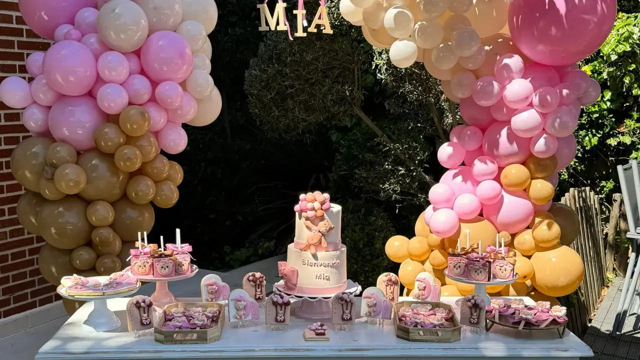 Mesa dulce baby shower con pastel de osito, galletas temáticas y globos rosas y dorados. ¡Bienvenida Mia!