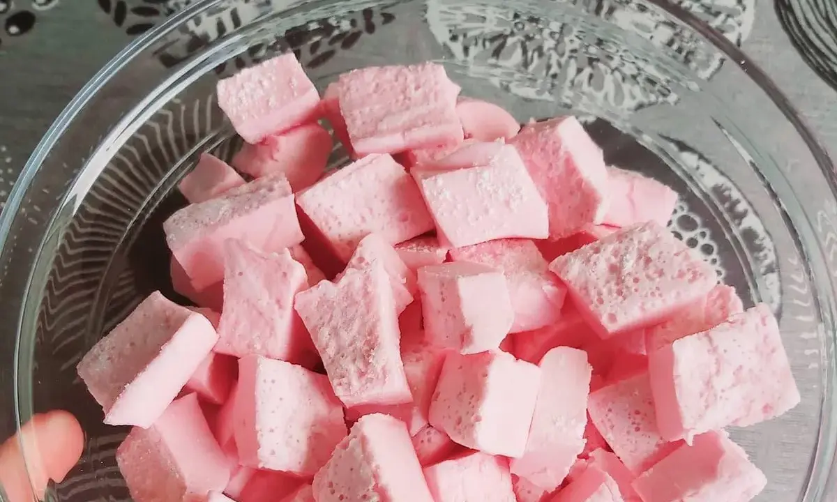 Nubes de golosina rosas cortadas en cubos en un bol de cristal, perfectas para recetas dulces.