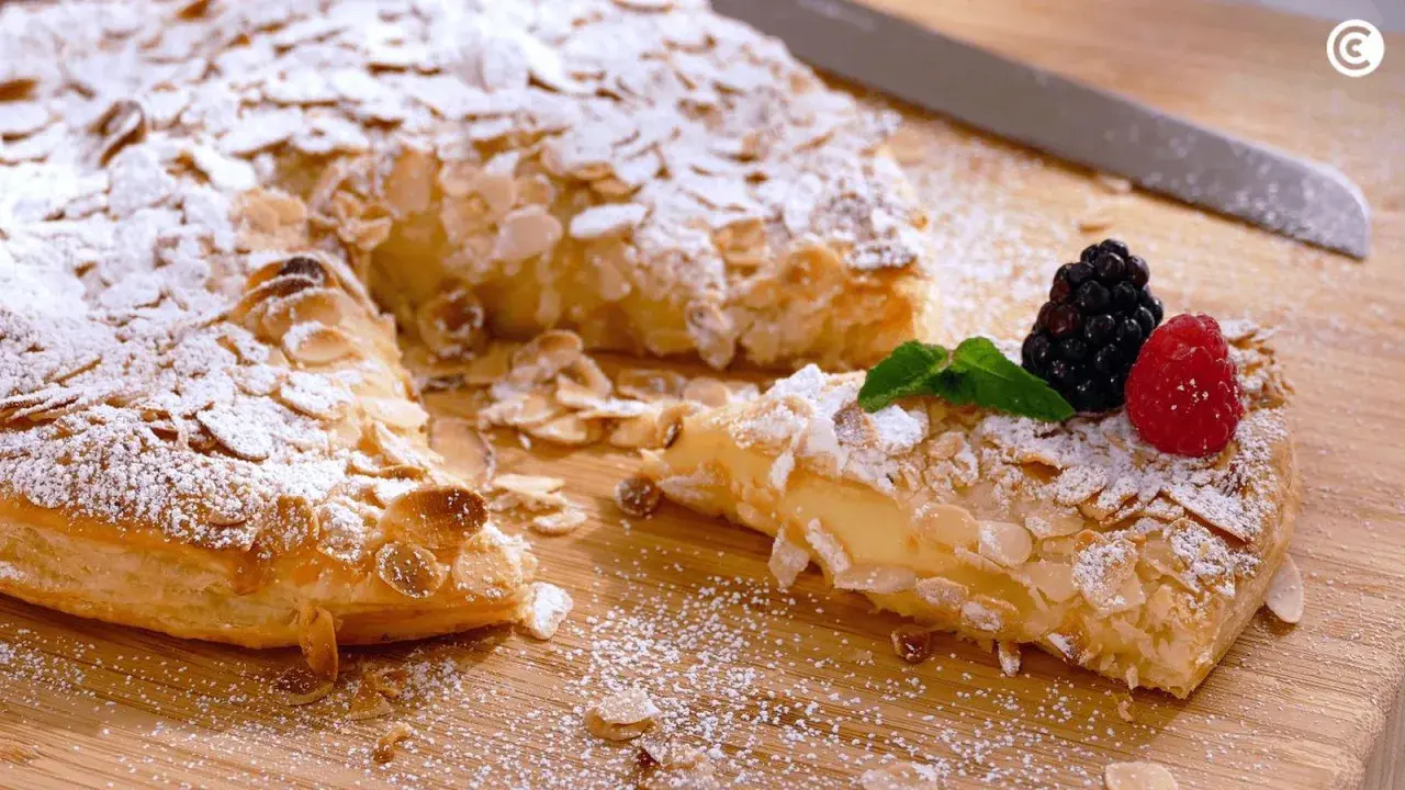 Deliciosos postres con hojaldre, cubiertos de almendras laminadas y azúcar glas. Una porción muestra un relleno cremoso y frutos rojos.