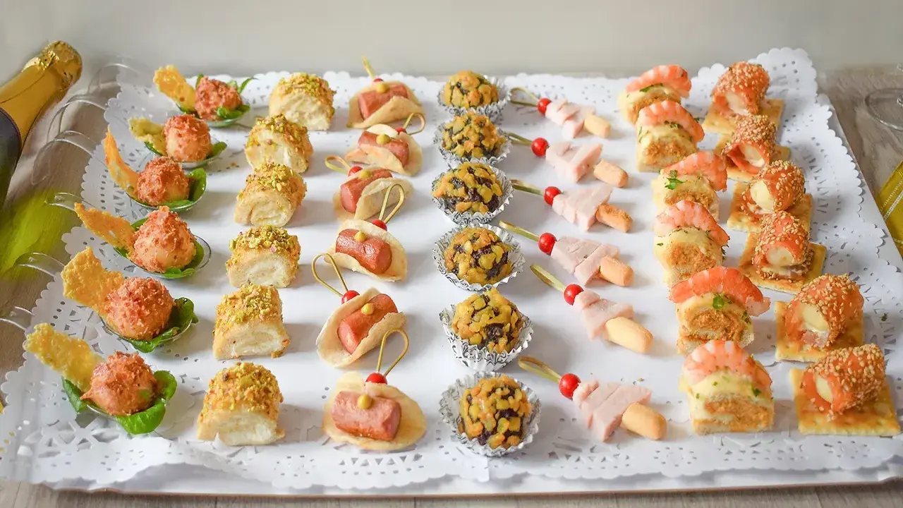 Bandeja con variedad de bocaditos salados, perfectos para un picoteo fácil y económico. Hay mini tacos, bolitas cubiertas de frutos secos, brochetas de jamón y canapés con gambas y salmón.