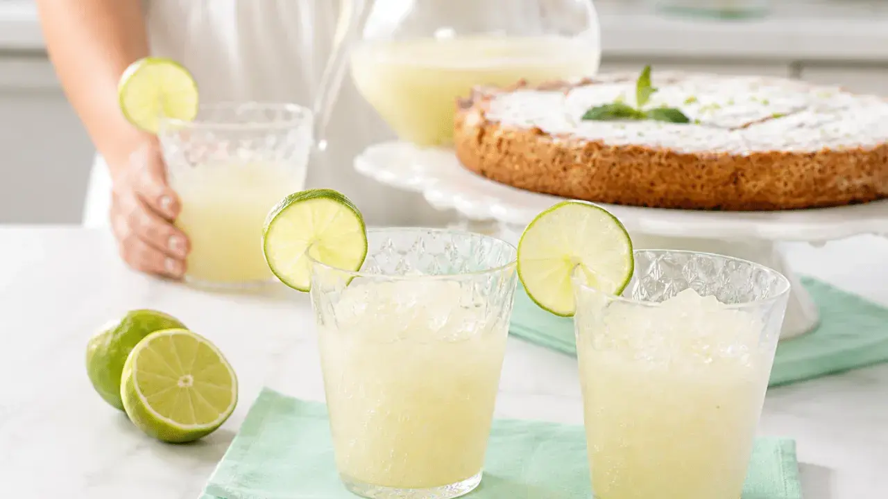 Refrescante granizado de limón Thermomix, perfecto para un día caluroso. Servido en vasos con rodajas de lima y acompañado de un delicioso pastel.