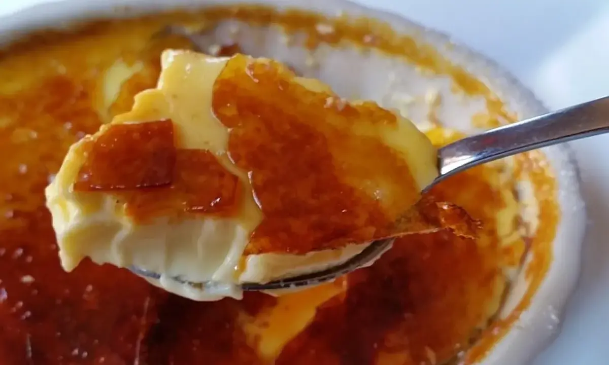 Cuchara levanta un trozo de cremoso creme brulee con su crujiente capa de caramelo tostado.