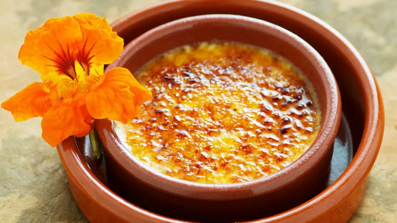 Crema catalana con una flor naranja. El postre tiene una capa de azúcar caramelizado crujiente.