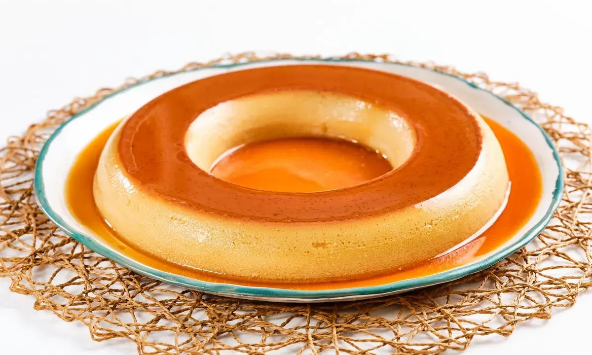 Un delicioso flan de café, con su caramelo dorado, reposa en un plato blanco con borde azul, sobre una esterilla tejida.