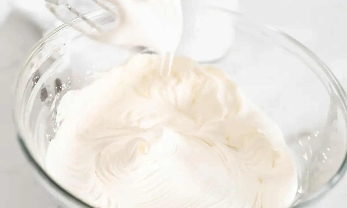 Batidora eléctrica batiendo para crear una deliciosa nata montada en un bol de cristal.