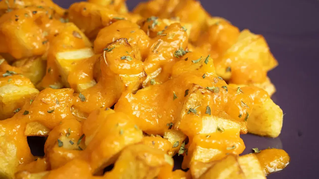 Patatas bravas receta: patatas fritas crujientes cubiertas con una salsa brava cremosa y hierbas picadas.