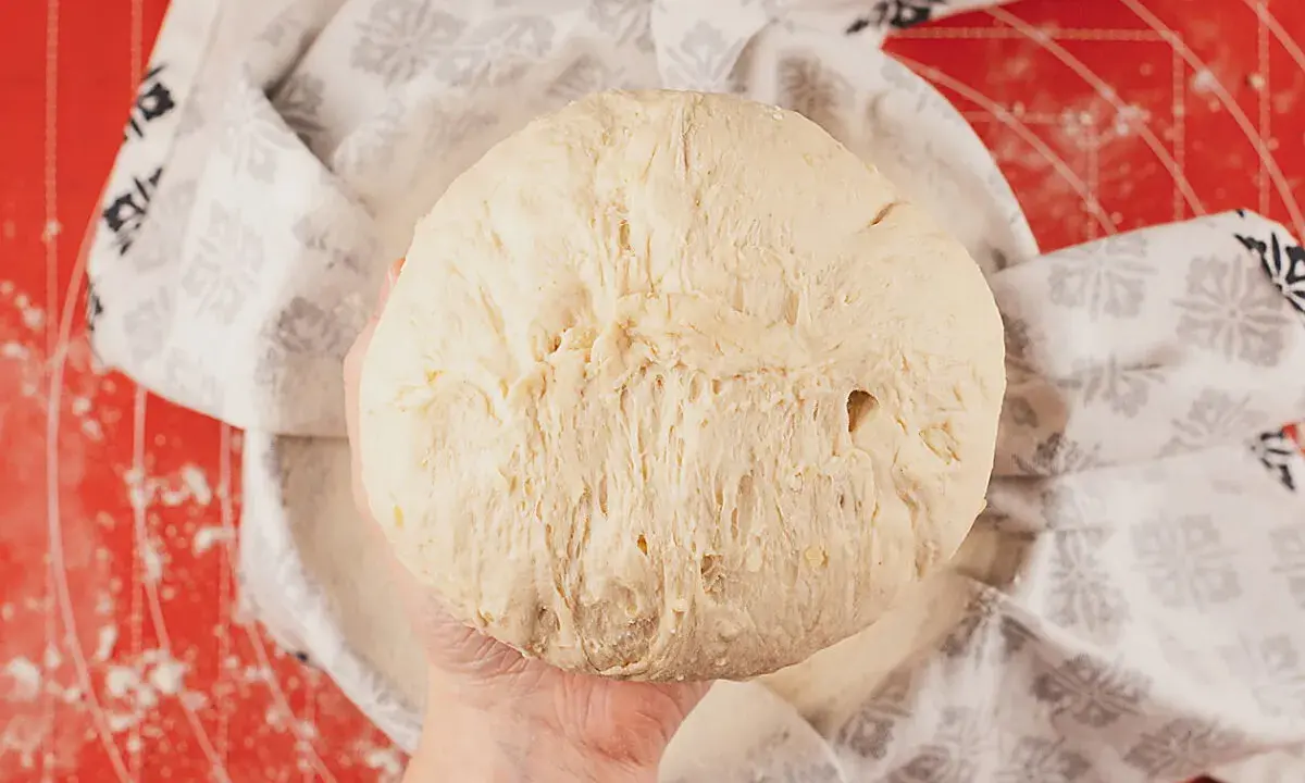 Masa de pan de patata esponjosa, lista para hornear, cubierta con un paño decorado.