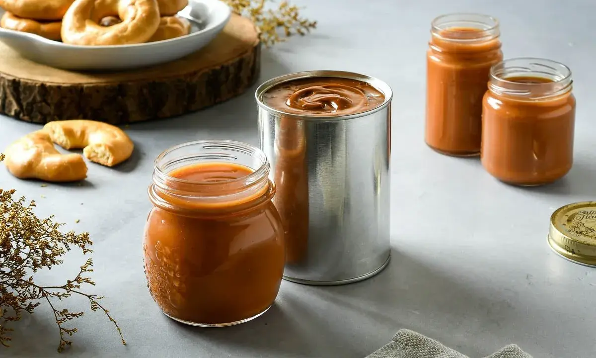 Dulce de leche receta: tarros y lata de dulce de leche, junto a galletas y decoración.