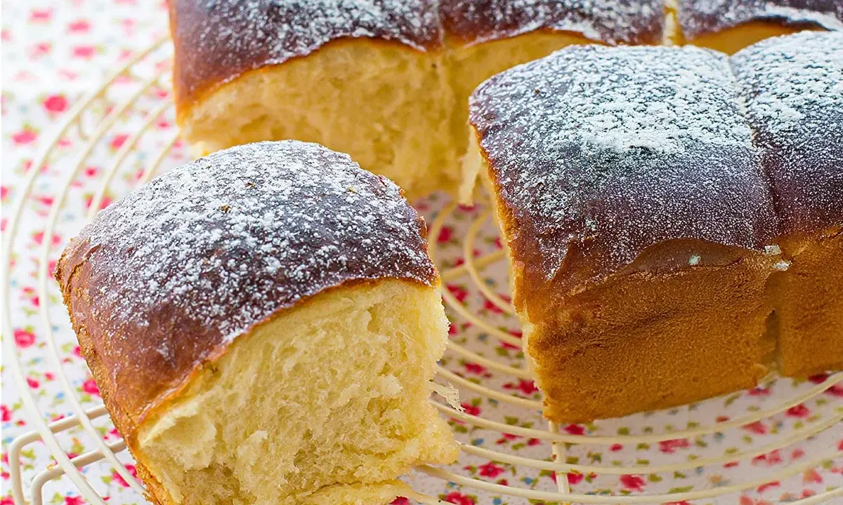 Pan brioche esponjoso y dorado, espolvoreado con azúcar glas sobre una rejilla.