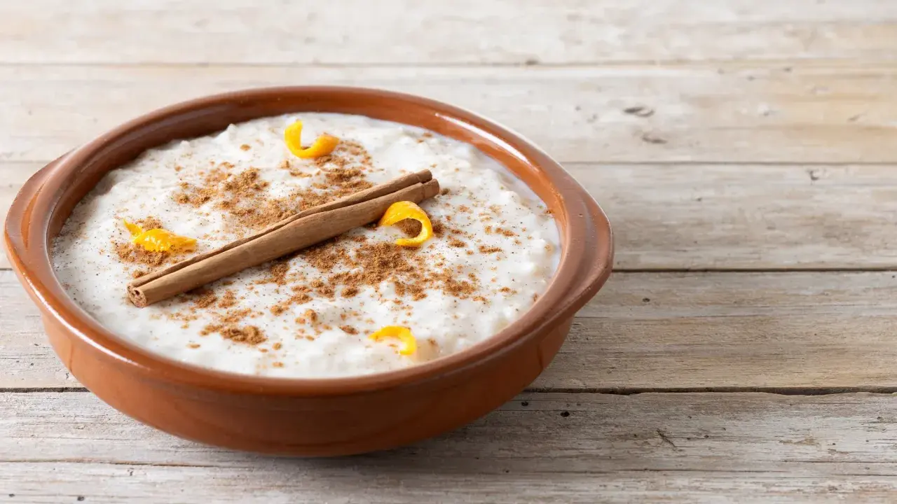Un tazón de arroz con leche cremoso, espolvoreado con canela y adornado con cáscara de naranja y una rama de canela.