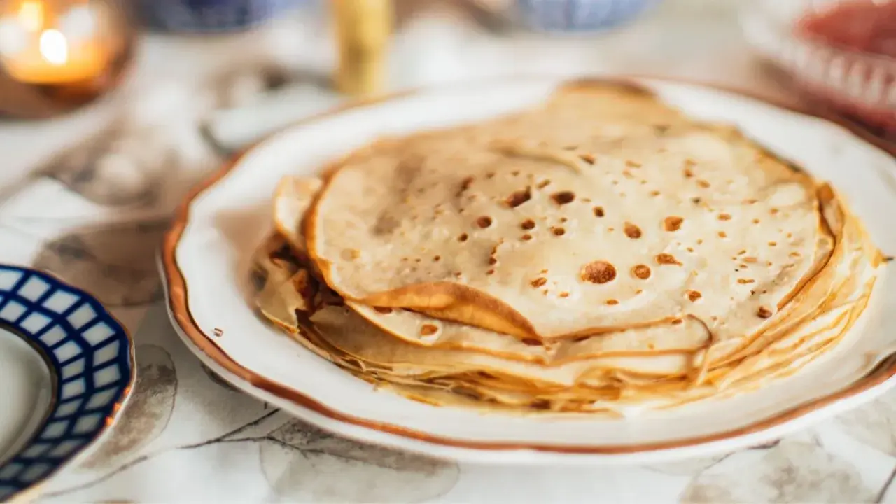 Una pila de masa crepes doradas y finas en un plato blanco.