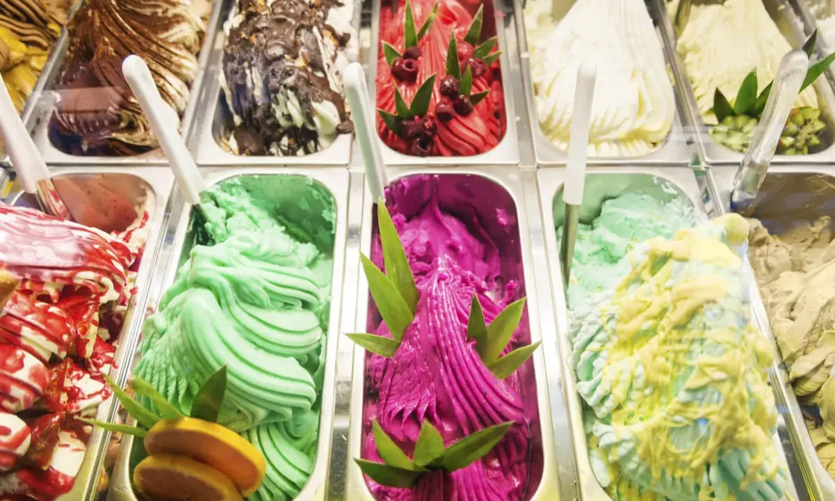 Variedad de helados cremosos, incluyendo un vibrante helado de pitahaya con azúcar invertida, decorado con hojas verdes y frutos rojos.