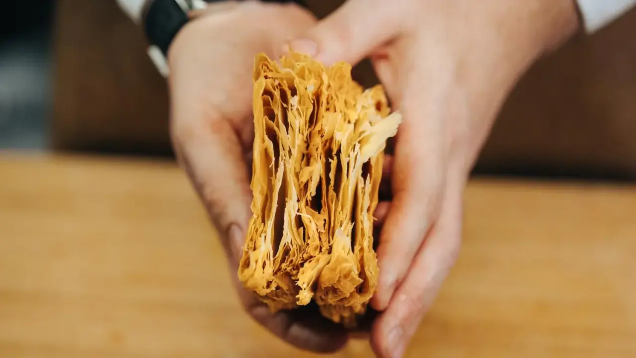 Manos sostienen un trozo de hojaldre casero, mostrando sus finas y crujientes capas doradas.