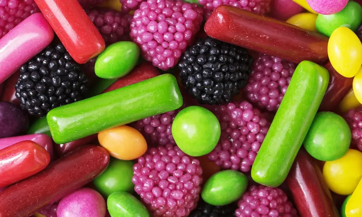 Un surtido vibrante de chuches, mostrando cómo se hacen las chuches con formas de bayas, bastones y pastillas en tonos rojos, verdes, morados y amarillos.