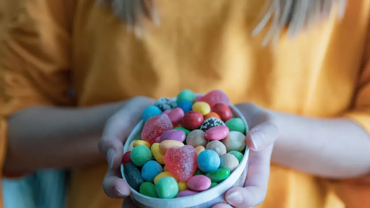 Manos sostienen un cuenco lleno de chuches saludables para niños: gomitas de corazón, bolitas de colores y más.