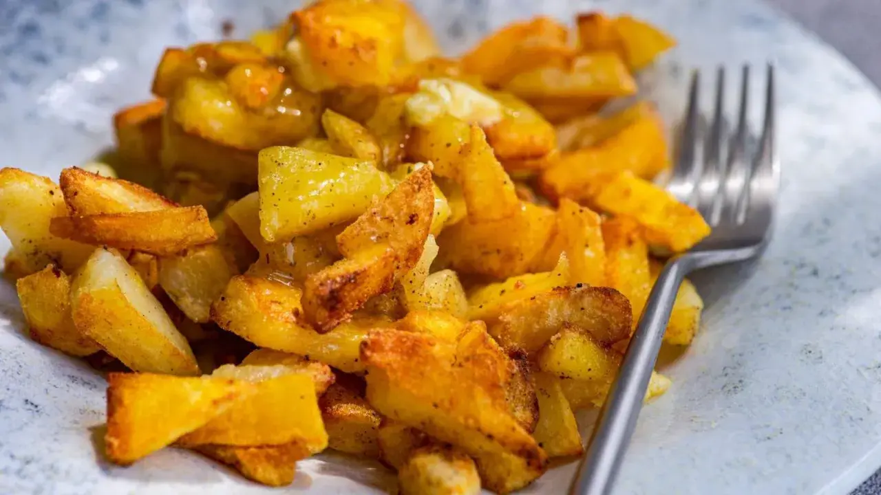 Patatas fritas al horno doradas y crujientes, sazonadas con especias, listas para disfrutar con un tenedor.