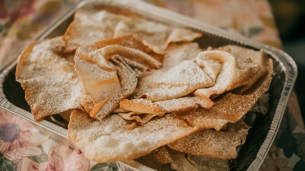 Orejas de carnaval espolvoreadas con azúcar glas en una bandeja metálica. ¡Perfectas para tu receta!