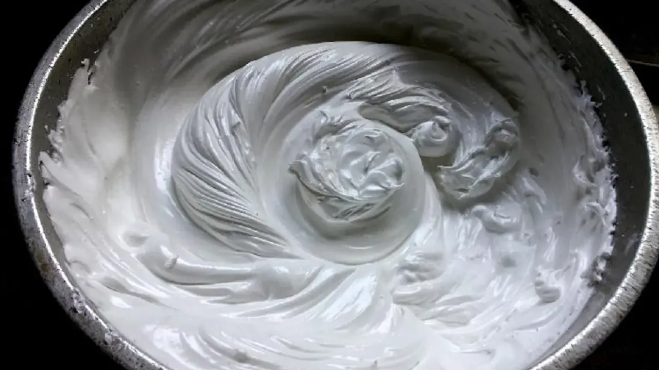 Merengue italiano recién batido en un bol metálico, con remolinos suaves y sedosos que invitan a probar su dulzura.