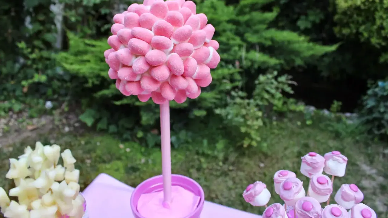 Un árbol de gominolas rosa, decorado con dulces, preside una mesa de fiesta al aire libre.