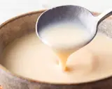 Cuchara sirviendo crema inglesa espesa y suave en un cuenco rústico.