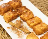 Deliciosa leche frita dorada y crujiente, espolvoreada con azúcar y canela, junto a una rama de canela.