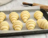 Ocho croissants caseros listos para hornear en una bandeja. Se ven deliciosos y prometen un gran desayuno.