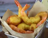 Crujientes gambas a la gabardina doradas, servidas en una cesta metálica con papel marrón.