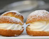 Dos bocados caseros de pasta choux, rellenos de crema batida y espolvoreados con azúcar glas.