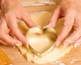 Manos cortan masa con un cortador en forma de corazón, parte de una receta de galletas caseras.