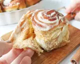 Un rollo de canela esponjoso, cubierto de glaseado cremoso, se separa suavemente.