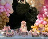 Mesa dulce baby shower con pastel de osito, galletas temáticas y globos rosas y dorados. ¡Bienvenida Mia!