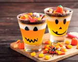 Deliciosa gelatina Halloween para niños, con capas de naranja y blanco, decorada como calabaza y cubierta de dulces.