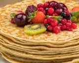 Pila de crepes dorados cubiertos con frutas rojas, fresas y kiwi. Una deliciosa receta crepes para disfrutar.