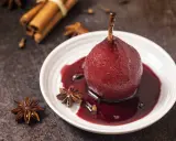 Peras al vino tinto, cocidas con especias como anís estrellado y canela, servidas en un plato blanco con su sirope.