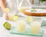Refrescante granizado de limón Thermomix, perfecto para un día caluroso. Servido en vasos con rodajas de lima y acompañado de un delicioso pastel.