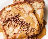 Tostadas francesas cubiertas con crema de cacahuete y crujientes bolitas de chocolate. Un desayuno delicioso y tentador.
