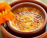 Crema catalana con una flor naranja. El postre tiene una capa de azúcar caramelizado crujiente.