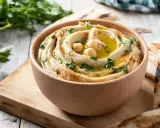 Hummus cremoso en cuenco de madera, decorado con garbanzos, aceite de oliva y perejil. Perfecto para aprender como hacer hummus casero.