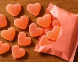 Dulces en forma de corazón, con un delicioso sabor a corazon de melocoton, esparcidos sobre una mesa de madera y saliendo de un paquete rosa.